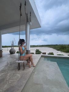 a woman sitting on a swing next to a swimming pool at Casa Almea Sisal in Sisal
