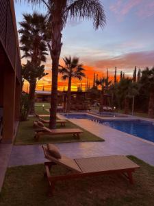 a sunset over a pool with benches and palm trees at Villa Sofia And Spa in Marrakech +12 photos