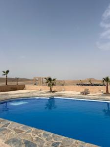 a blue swimming pool with palm trees in the desert at Amazigh van Agafay in Oumnas
