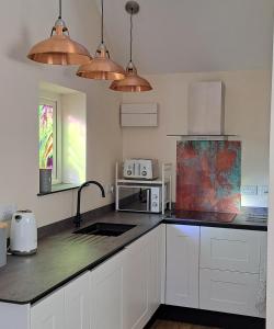 a kitchen with white cabinets and copper pendant lights at Ty Heulwen Studio in St. Davids