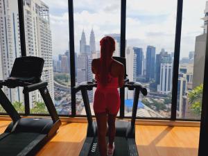 a woman in a red dress is on a treadmill looking out of a window at KLCC View City Center At Majestic residence in Kuala Lumpur