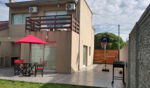 a patio with a table and a red umbrella and a basketball hoop at Casa alquiler temporal Santa Clara del Mar in Santa Clara del Mar