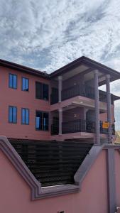 a large pink building with a balcony and columns at Cozy 2-bedrooms in Lakeside Estate Accra in Apenkwa