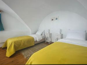 deux lits dans une chambre blanche avec des draps jaunes dans l'établissement Sunset Aura Santorini, à Éxo Goniá