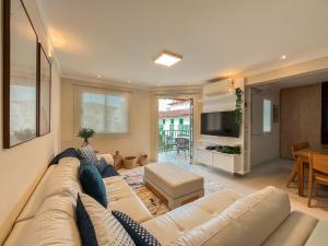 a living room with a white couch and a television at Riviera - Duplex Lindo Contemporâneo com Enxoval Completo in Riviera de São Lourenço