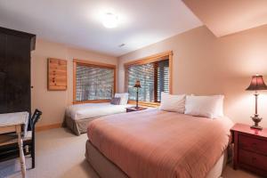 a bedroom with two beds and a desk and two windows at Heron Chalet by Outpost Whistler in Whistler