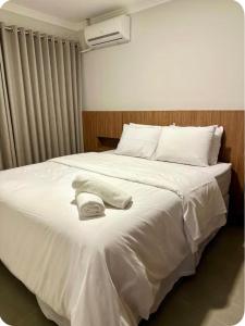 Una cama blanca con un sombrero encima. en Apartamento aconchegante próximo ao mar em Itapoá, en Itapoa