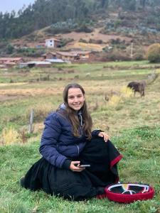 une femme assise dans l'herbe avec un téléphone portable dans l'établissement Cabañas lago piuray, à Chincheros