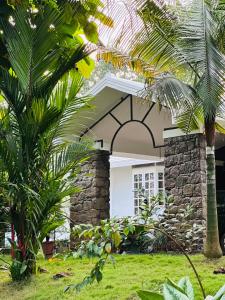 a house with a stone wall and palm trees at The Mallika Holidays in Mananthavady