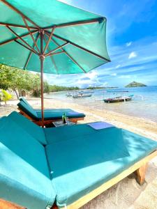 a bench with an umbrella on the beach at Golden Beach Hotel Lombok in Pulau Gilipoh