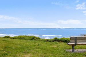 a bench sitting on top of a grassy hill overlooking the ocean at Wow On Wanaka Bay - beachfront living at its best in New Plymouth