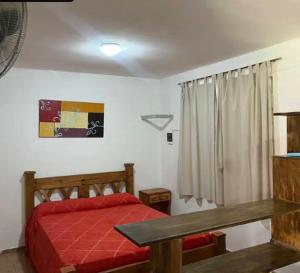 1 dormitorio con cama roja y mesa en Departamentos Turísticos, en Cosquín