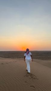 a woman walking in the desert with the sun in the background at Alghyamcamp in Muntarib