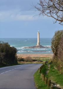a road with a lighthouse in the ocean next to a street at Chambre phare in Auderville +5 photos