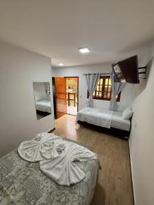 イーリャ・グランデにあるSuítes Refúgioのベッドが2つと壁にテレビがある寝室