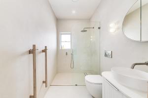 a white bathroom with a shower and a sink at Beachfront 1 Bed across from iconic BONDI BEACH in Sydney +11 photos