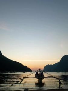 a person walking on the beach with a boat in the water at El Nido Cabugao Loudge in El Nido