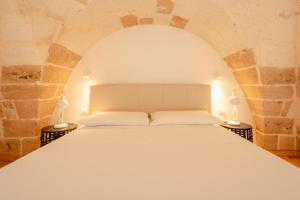 a bedroom with a white bed in a stone wall at Le Casine di Maruggio Albergo Diffuso in Maruggio