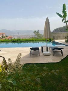 a pool with a table and an umbrella and two benches at Stylish Lounge Apartment with Pool & Views in Fethiye