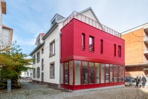 Un bâtiment rouge avec des gens qui marchent devant lui dans l'établissement Chez Arlette - Neuf - Haut de Gamme - Tram - Proche centre-ville - Tout confort, à Strasbourg