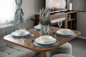a wooden table with plates and wine glasses on it at Seton Sands-3 Bed Static Caravan in Port Seton