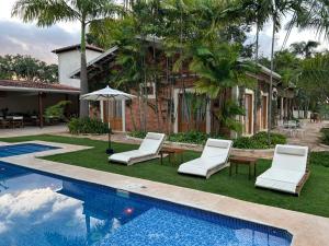 a villa with a swimming pool and chairs and a house at Pousada Manacá Exclusive Suítes in Rifaina