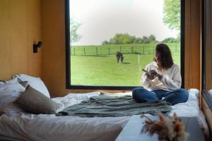 a woman sitting on a bed looking at a book at Parcel Tiny House I L'Arche des Hays in Les Hays