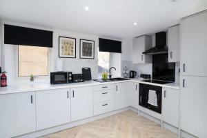een witte keuken met witte kasten en zwarte apparaten bij Modern 5 BED-2 BATH Apartment in Galashiels