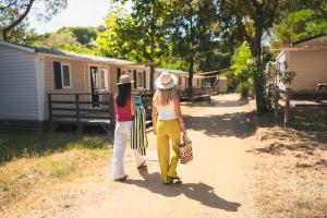 two women walking down a dirt road towards a cabin at HolaCamp Palamós in Vall-Llobrega