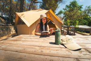 a woman sitting in a dog house with a book at HolaCamp Palamós in Vall-Llobrega
