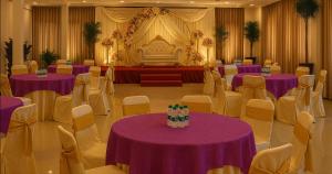 a banquet hall with purple tables and chairs and a stage at The Royal Oak in Bhatkal