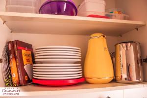 a shelf with a bunch of plates and books at MELHOR ESCOLHA - 2 Quartos com AR CONDICIONADOS SPLIT, Air Fryer, Wi-Fi, Disney Plus, Star Plus, HBO Max, Cadeiras de Praia, Caixa Térmica - 7 pessoas - Localização Nobre - CONFORTO Máximo! in Guarapari