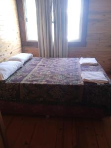 a bed in a wooden room with two windows at Las Cabañas in Las Grutas