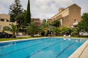 a swimming pool in front of a building with palm trees at Hotel Antiga in Calafell