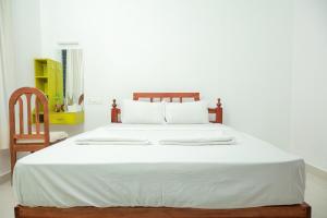 a large bed with white sheets and a wooden chair at Lakshmi Ayurveda & Yoga Apartment in Kovalam