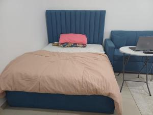 a bed with a blue headboard and a laptop on a table at Shared Studio in a marvel location and marvel furniture in Abu Dhabi Center in Abu Dhabi