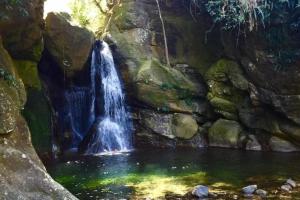 a waterfall in a pool of water next to a rock wall at Pousada Magia da Aldeia in Silva Jardim