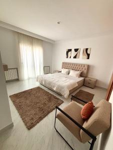 a white bedroom with a bed and a chair at Le somptueux du lac 2 in El Aouina Station