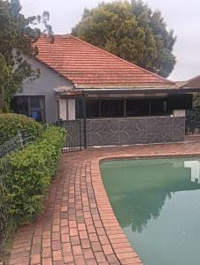 Coty and Reuben's guesthouse في جوهانسبرغ: منزل به ممشى من الطوب بجانب مسبح