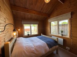 a bed in a wooden room with two windows at The Cabin 6 minutes from the Eurotunnel in Folkestone