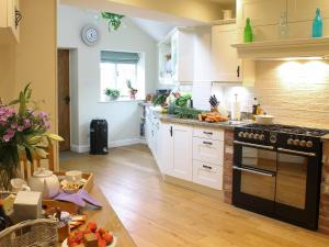 eine Küche mit weißen Schränken und einem schwarzen Herd mit Backofen in der Unterkunft Pond View Cottage in Brantingham