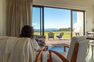 a woman sitting in a chair reading a book in a living room at Harvest Rise Vineyard Cottage in Pahautea