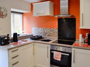 a kitchen with white cabinets and an orange wall at Stable Cottage in Penrhyn Bay