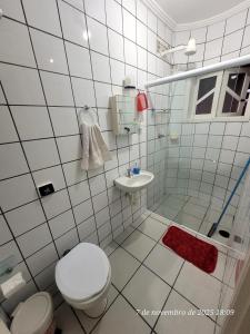 ein weiß gefliestes Badezimmer mit Toilette und Waschbecken in der Unterkunft Casa em Caraguá, uma quadra da praia com ar in Caraguatatuba