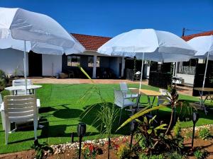 eine Terrasse mit Tischen, weißen Stühlen und Sonnenschirmen in der Unterkunft Shado's residence self catering cotages in Serowe