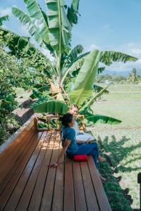 two women sitting on a wooden deck under a palm tree at Mantra Yoga Homestay in Tanjung