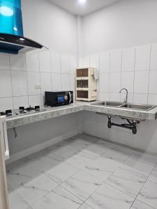 a white tiled kitchen with a sink and a microwave at Cozy Corner in Samut Prakan