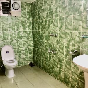 a green tiled bathroom with a toilet and a sink at Maya Eco Guest House in Dhaka