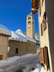 ein Gebäude mit einem Uhrturm mit Schnee darauf in der Unterkunft Maison Patou, superbe duplex au coeur du village du Casset, Le Monêtier les Bains, Serre Chevalier in Le Casset