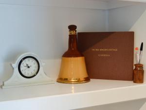 une bouteille et une horloge sur une étagère avec une boîte dans l'établissement The Bellringers Cottage, à Llandegla